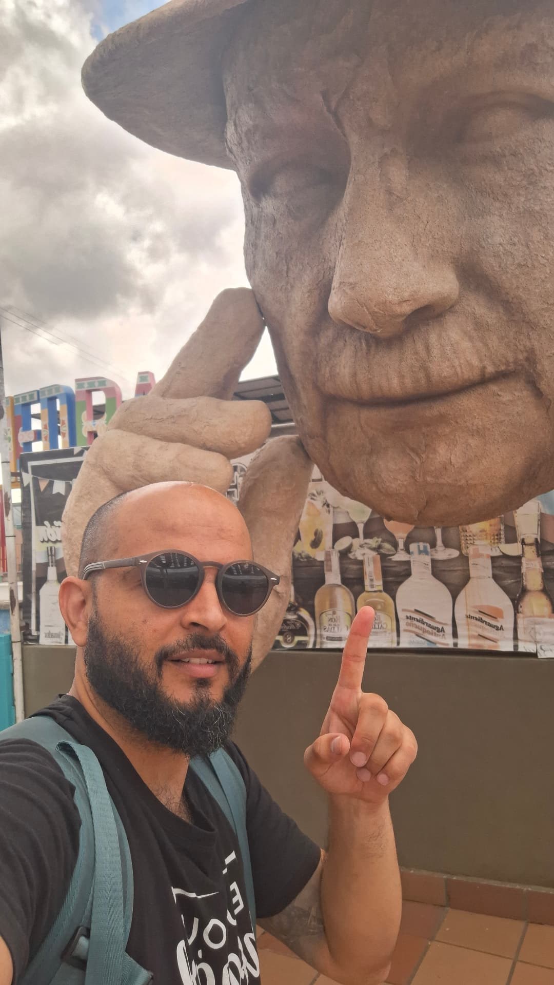 Tiago diante de uma escultura de rosto com chapéu na Colômbia