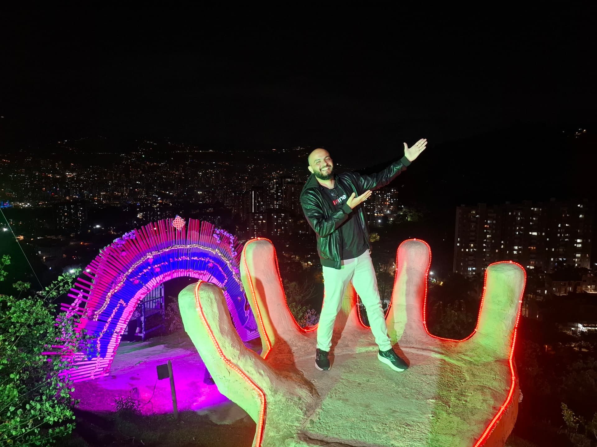 Tiago sobre uma escultura de mão iluminada à noite na Colômbia